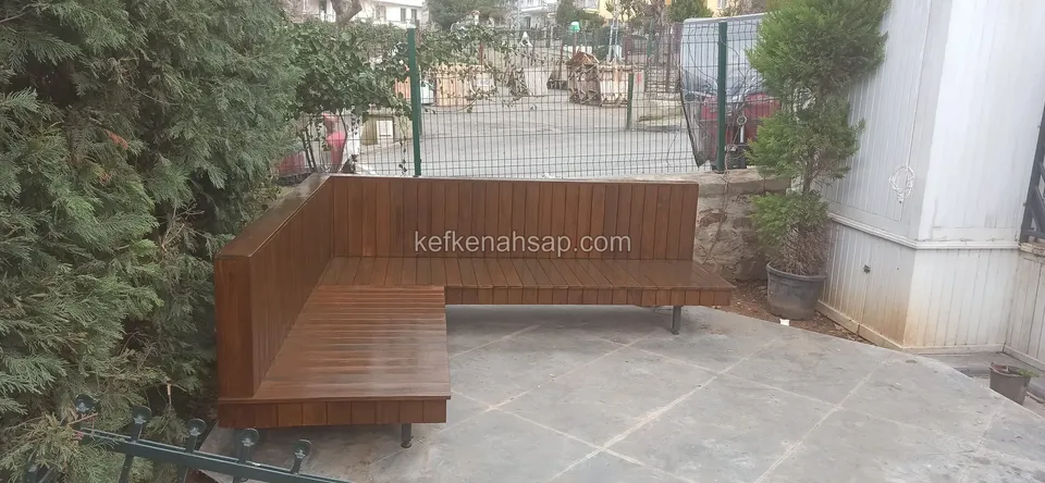 A dark-varnished L-shaped timber seating unit raised on thin metal legs in a stone-paved garden