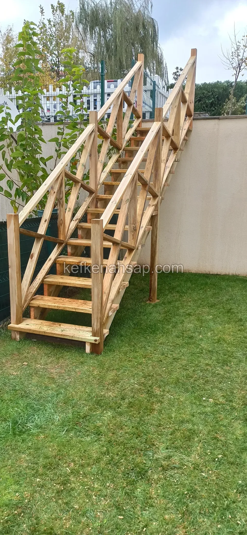 Honigfarbene Holztreppe mit Diagonalgeländer, die auf dem Rasen parallel zur Mauer ansteigt