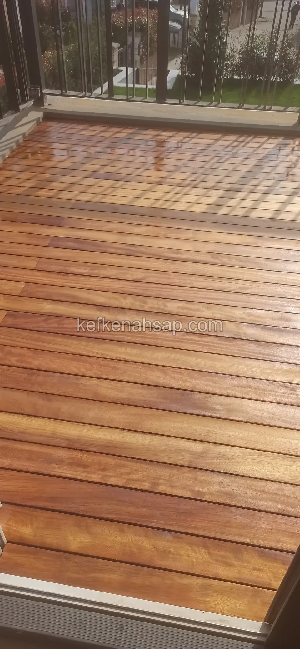 Demir korkuluklu bir terasın zemininde, altın kahve tonlu ve parlak yüzeyli yeni yağlanmış deck tahtaları