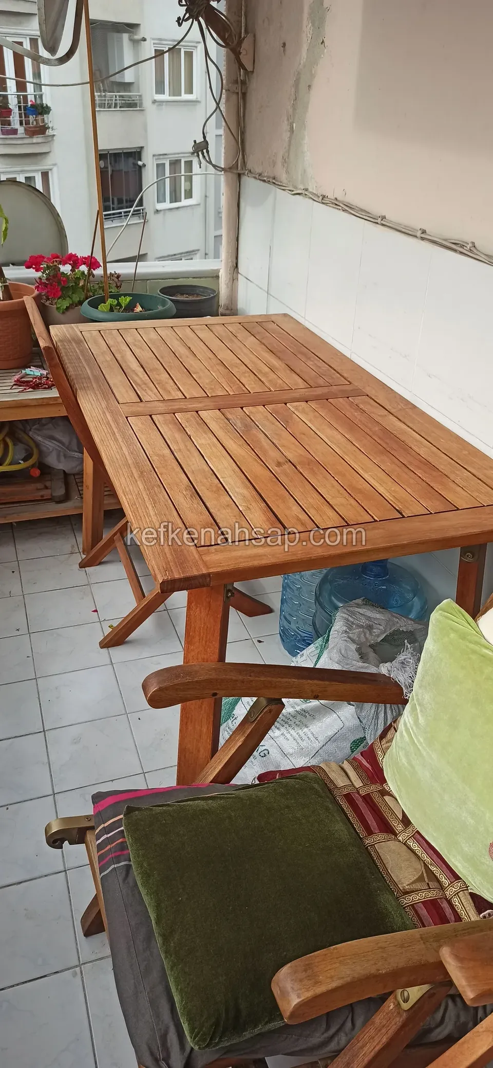 On a tiled balcony, a long slatted timber table with a timber chair holding a green cushion in front