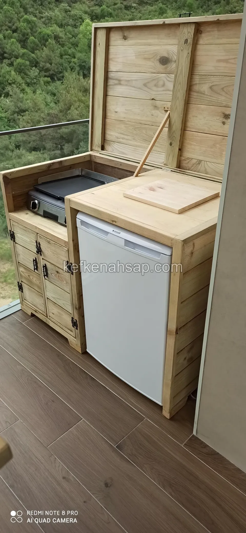 Balkon zemininde, ocak ve mini buzdolabı yerleştirilmiş, kapaklı ahşap dolaplardan oluşan açık mutfak
