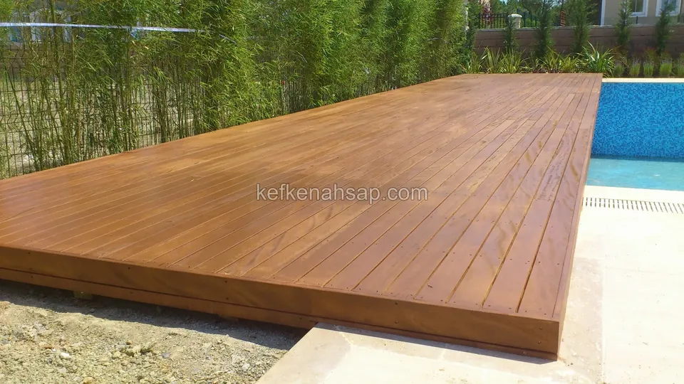 Bambu dizisinin önünde, havuz kenarına uzanan düz yüzeyli koyu tonlu ahşap deck
