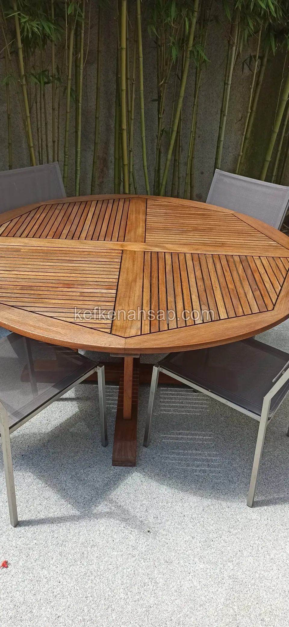 Vor einem Bambusvorhang steht ein runder Holztisch mit keilförmig verlegten Latten