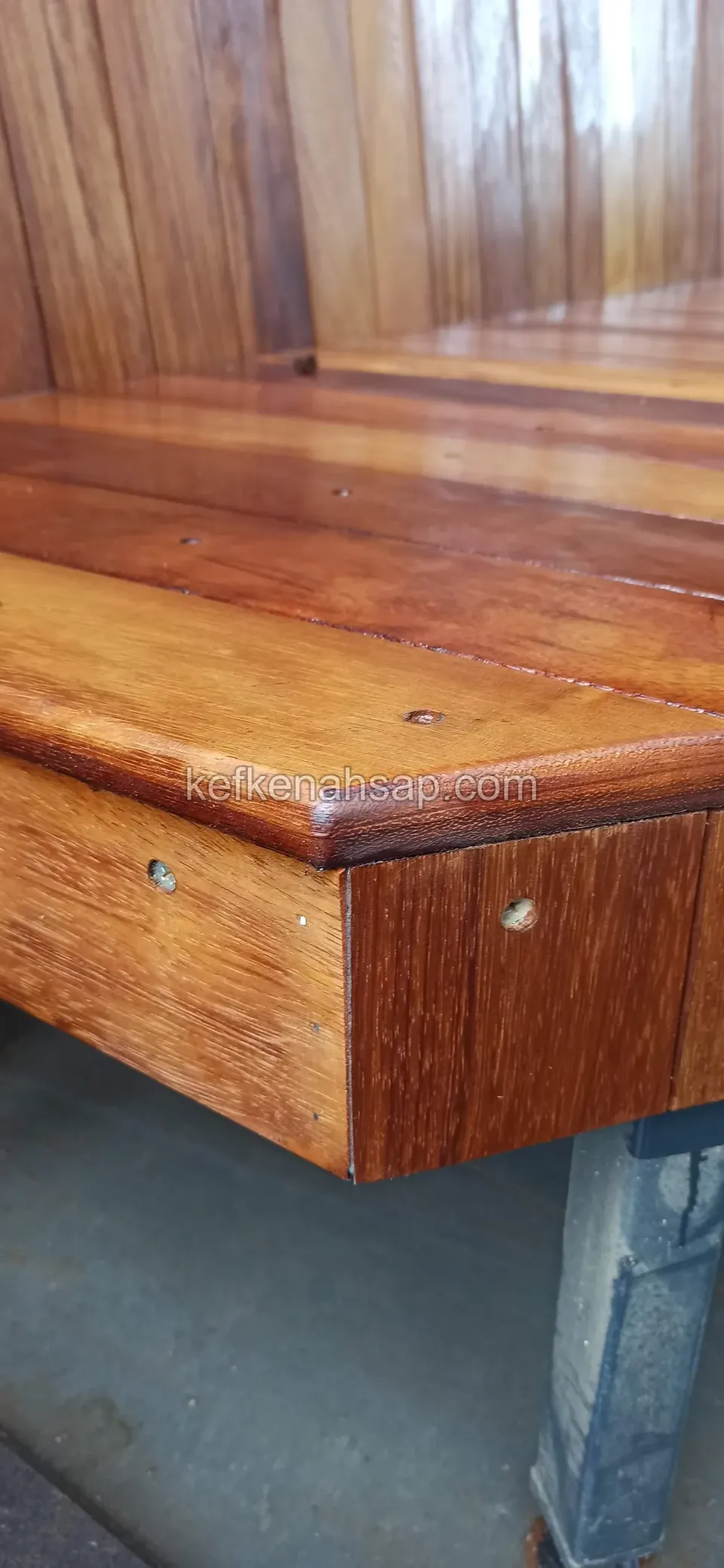 Nahaufnahme der Eckkante einer glänzend lackierten Holzbanksitzfläche mit kleinem