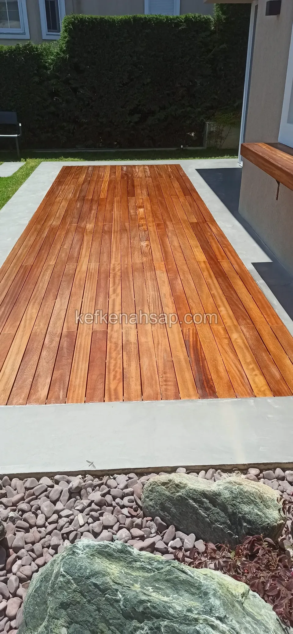 Beton çerçeve içine döşenmiş, çakıl ve kayalı bahçe düzenlemesinin yanında parlak ahşap deck