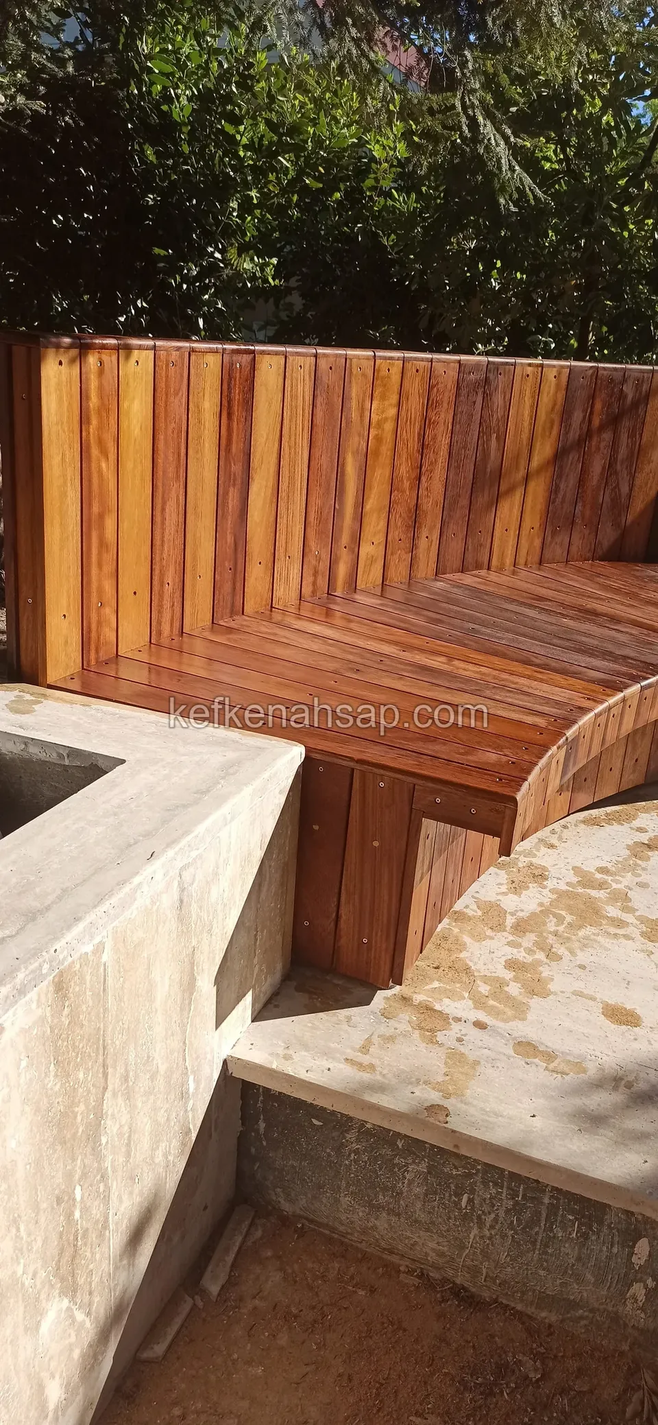 Eine Bank mit senkrechter Holzlehne und holzbelegter Sitzfläche auf einer geschwungenen Betonstruktur