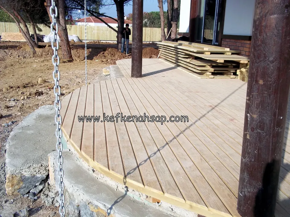 Pale deck with a rounded outline, ringed by a concrete edge strip, with a post hung with a chain and stacked boards beside it