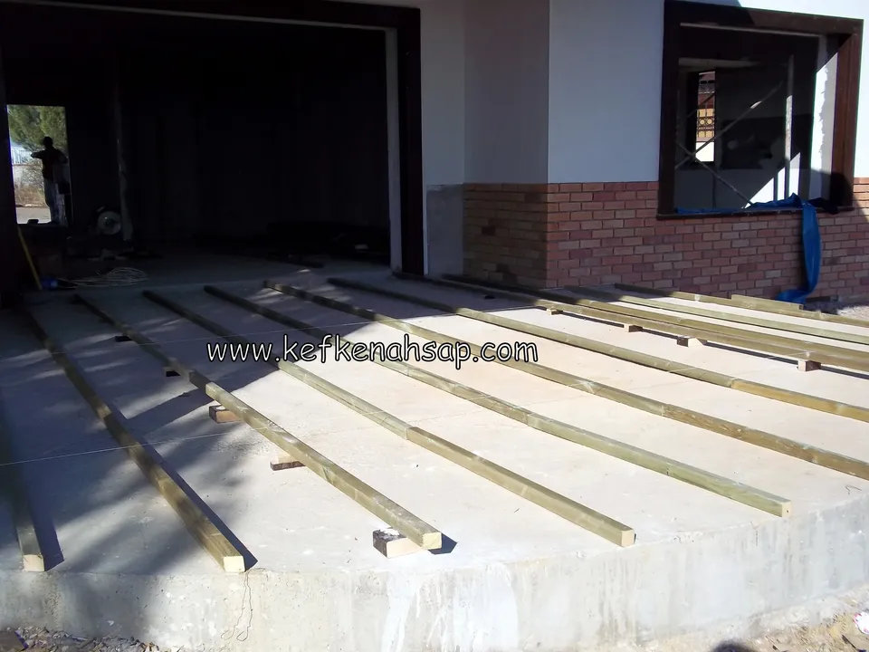 Pressure-treated timber support joists set out at an angle over a concrete floor, with no deck boards yet
