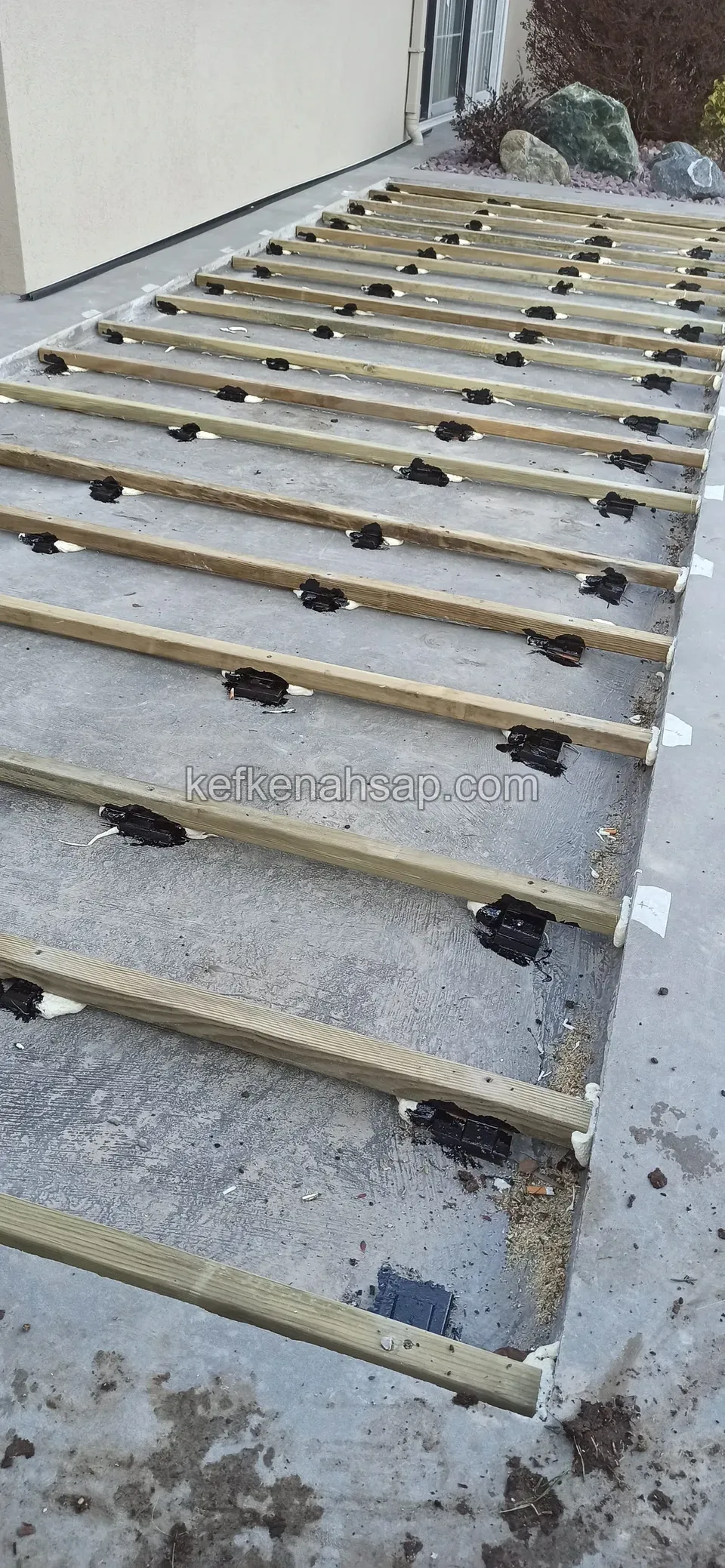 Eğimli beton yüzeyde plastik ayaklar üzerine dizilmiş emprenyeli çam kirişler, yerde çamur izleri