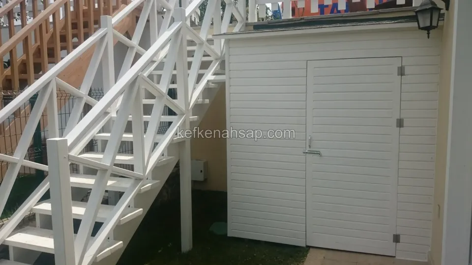 Beyaz boyalı ahşap dış merdiven korkuluğu ve merdiven altındaki yatay kaplamalı, beyaz depo kapısı
