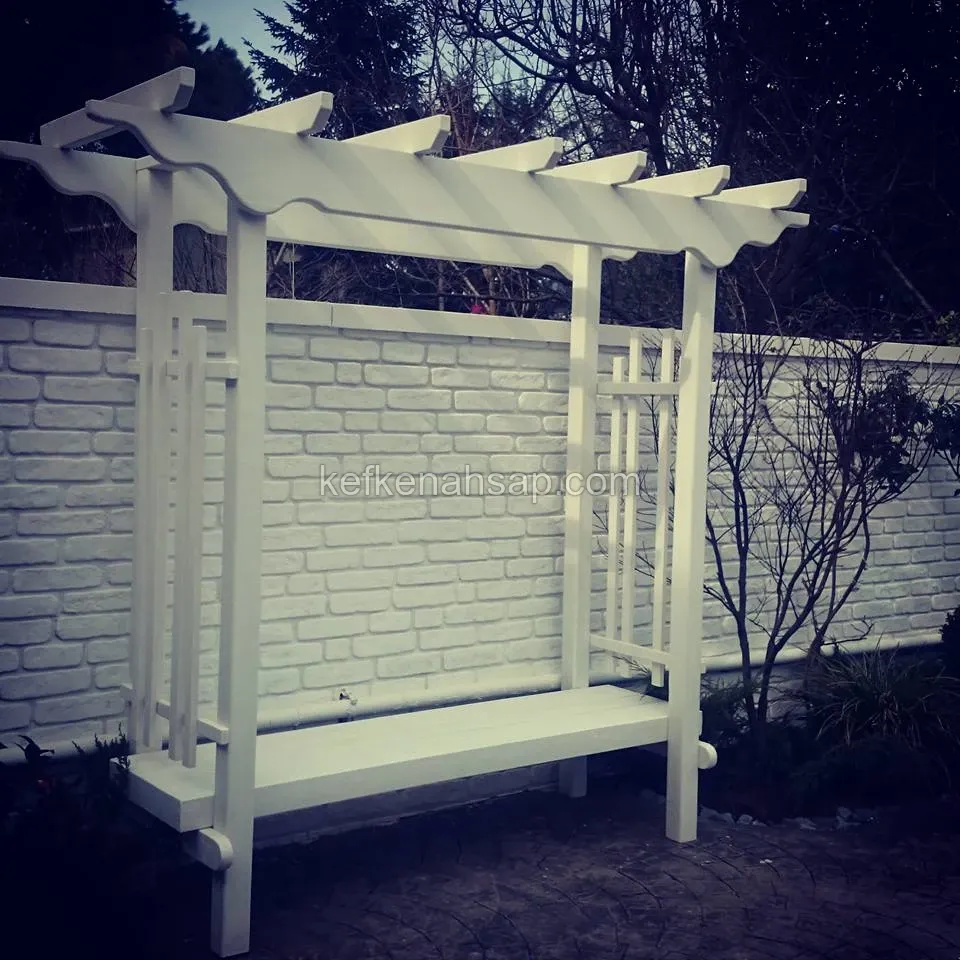 White painted wooden pergola with a built-in bench, standing in front of a white brick-pattern garden wall
