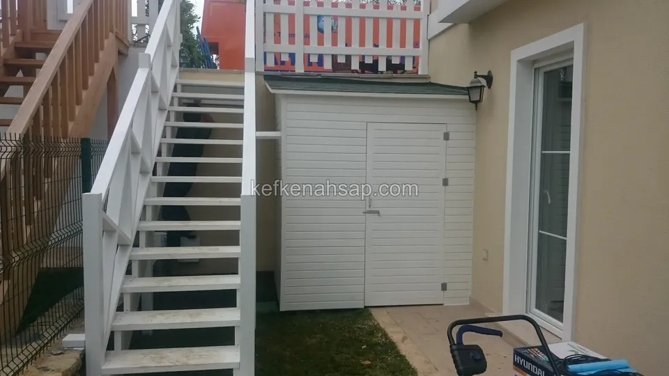 Beyaz boyalı açık basamaklı ahşap merdiven ve altına yerleştirilmiş beyaz çift kapaklı depo; yanda evin cam kapısı