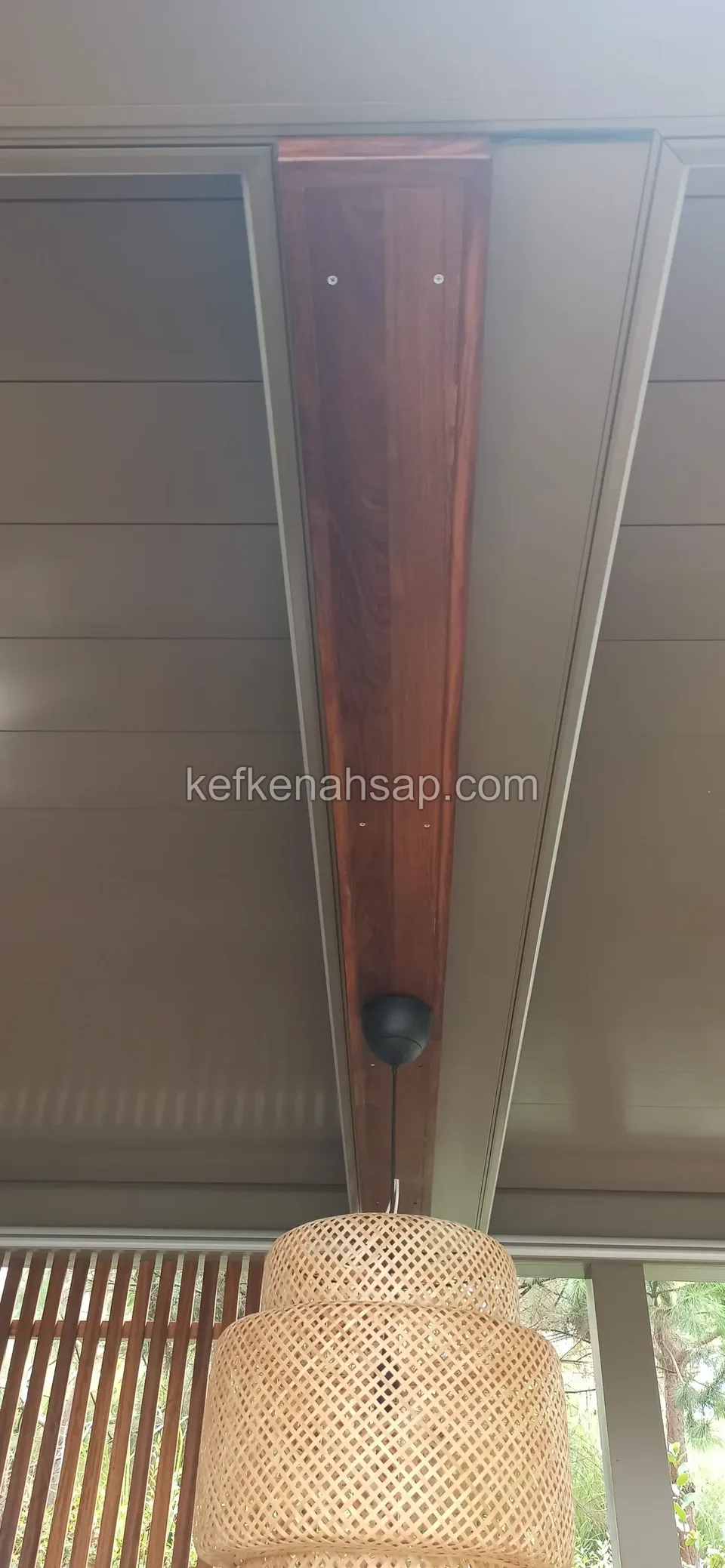 Beyaz çatı panellerini bölen koyu renkli ahşap kiriş; altında asılı hasır avize