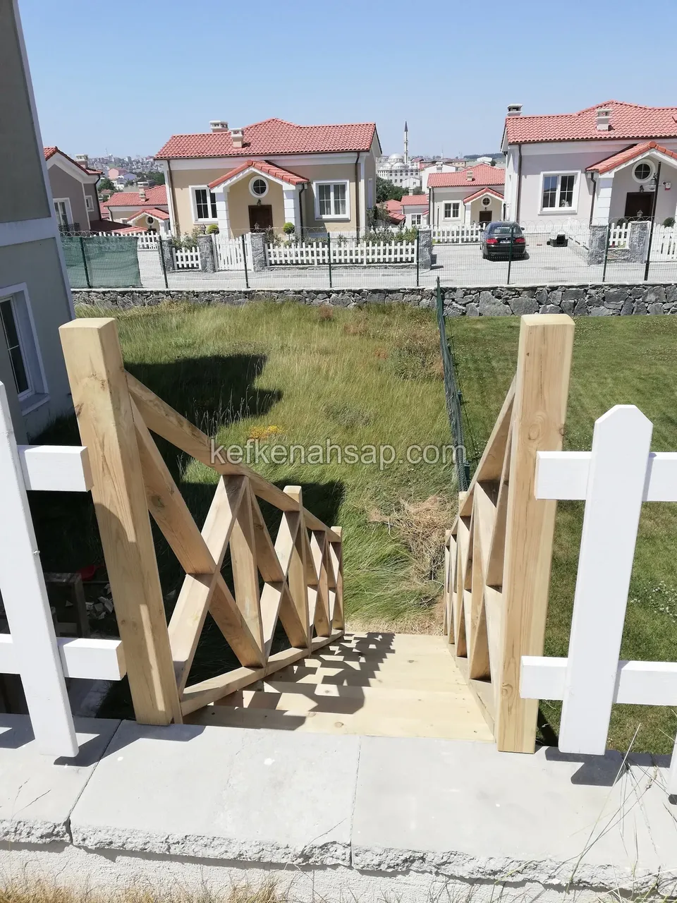 Holztreppe mit Kreuzstreben-Geländer, die durch einen weißen Zaun in den Garten hinabführt