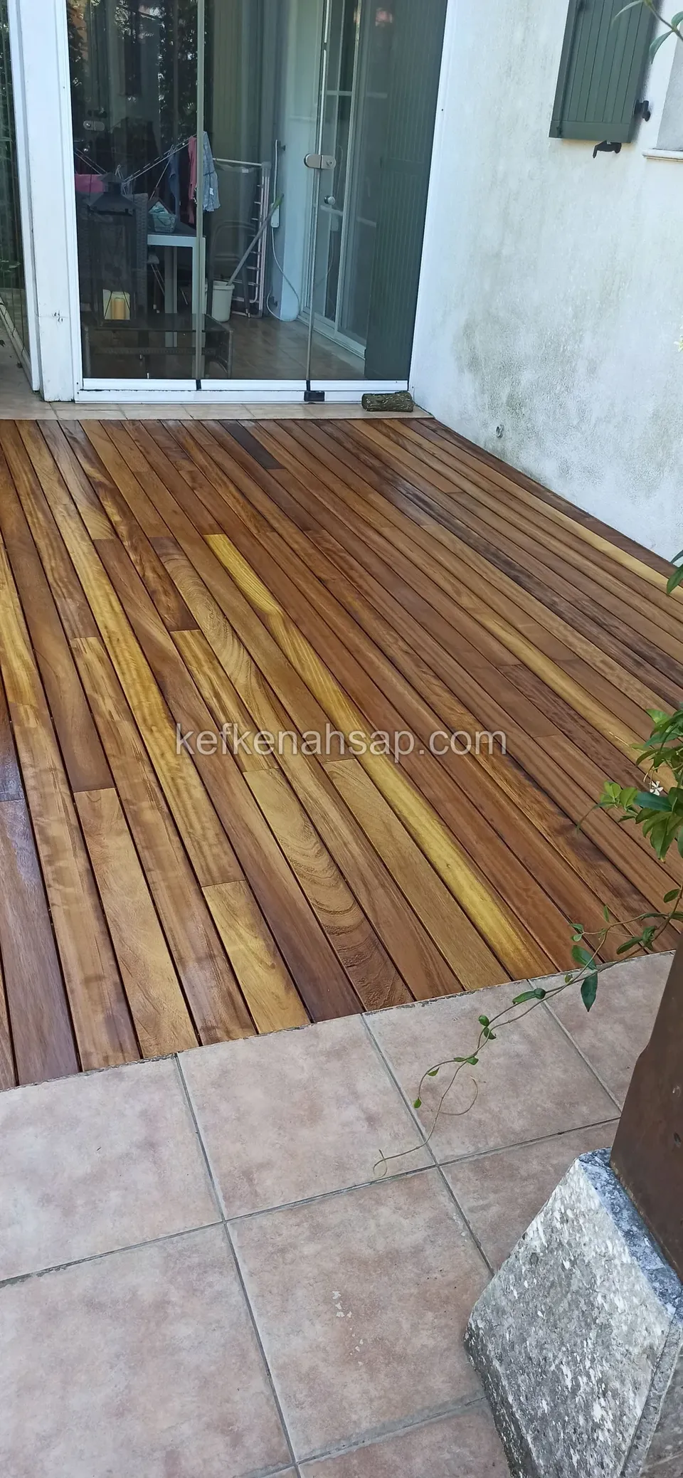 Varnished deck in front of a white-painted wall and a shuttered glass door, joined to the tiled floor