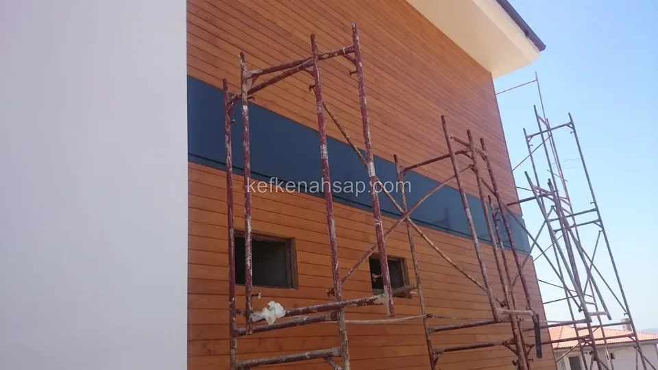 Beyaz duvarın yanında iskeleli, yatay ahşap kaplamalı bina cephesi
