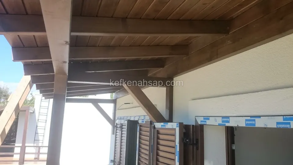 Beyaz duvarın önünde, koyu vernikli lambri tavanlı ahşap çatı; kapıların etrafı henüz bitmemiş