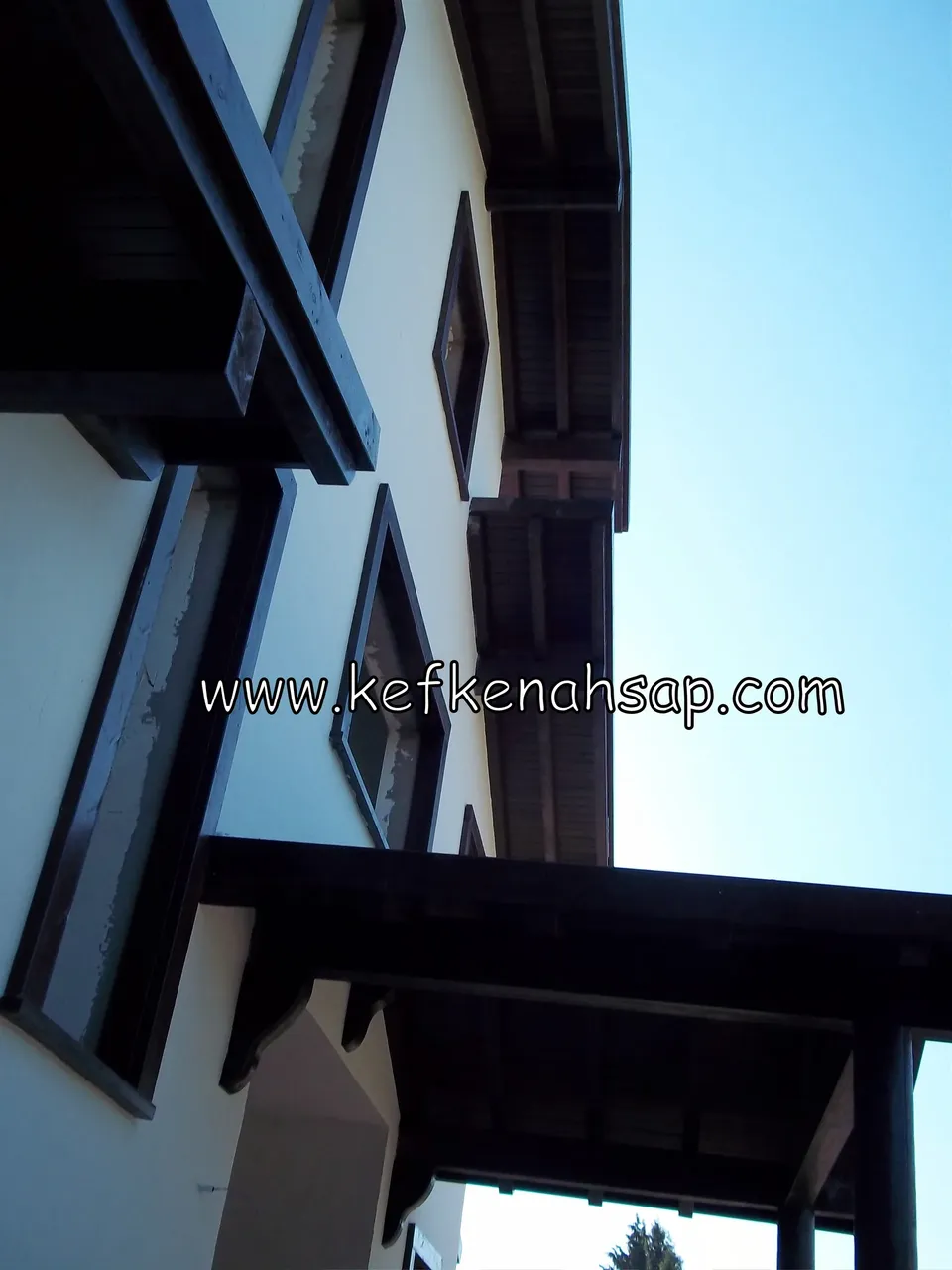 Beyaz boyalı duvarlı binada koyu ahşap çatı saçakları, balkon altı ve pencere çerçeveleri