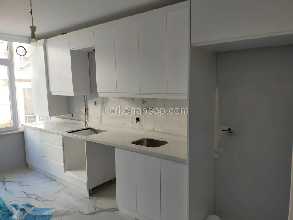 Montajı süren beyaz kapaklı alt ve üst mutfak dolapları ile açık renk tezgah.