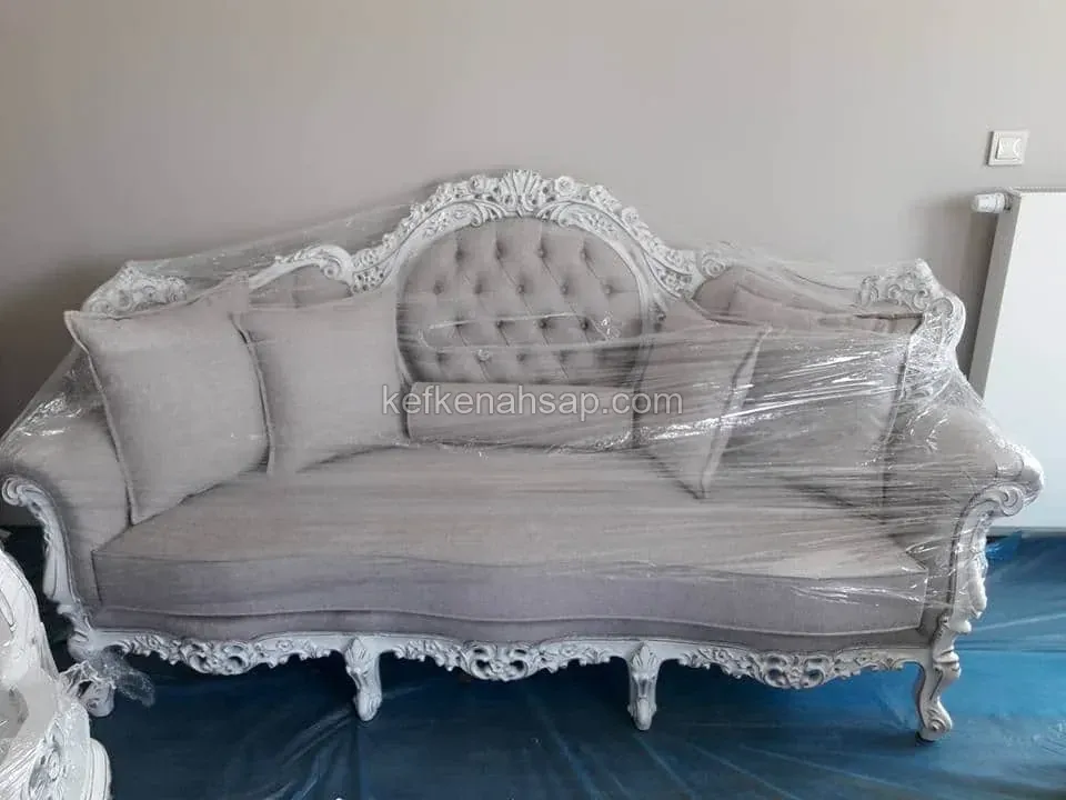 Classic sofa with white-painted carved wooden frame and grey tufted back, wrapped in film on a blue plastic-covered floor