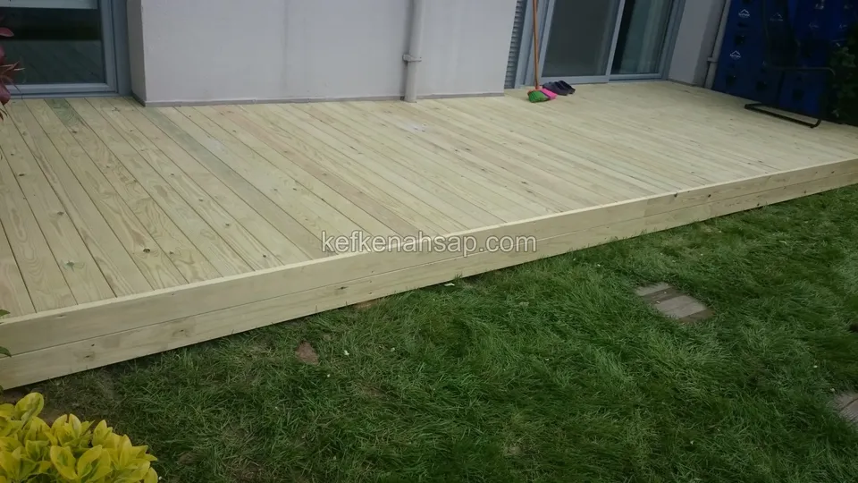 Zemin kat dış duvarı boyunca çimenin üzerine döşenmiş açık renkli emprenyeli çam deck platformu