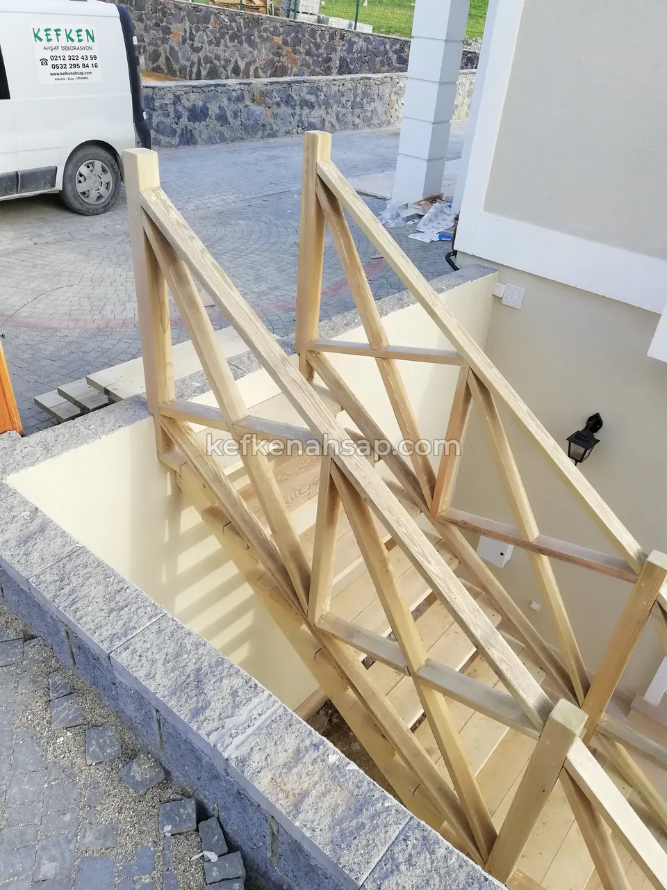 Holztreppe mit Kreuzstreben-Geländer hinab zum Kellereingang eines Hauses, Steinmauer und ein geparktes Fahrzeug im Blick