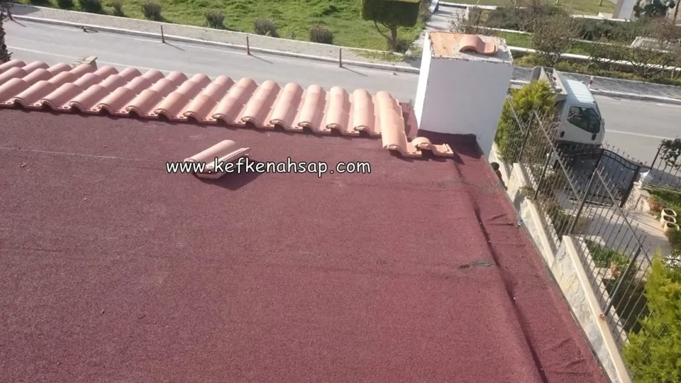 Bordo kaplamalı çatı yüzeyinde kenar boyunca dizilmiş kiremitler, yanda beyaz baca ve arkada sokak