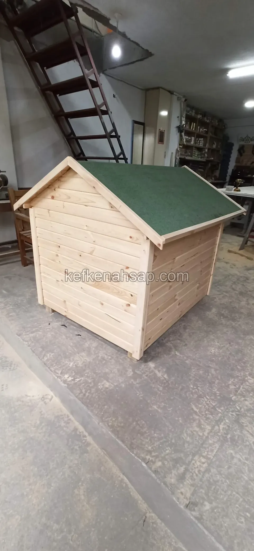 Boyasız ahşap yatay kaplamalı, yeşil çatılı köpek kulübesi; yan görünüm ve arkada atölye