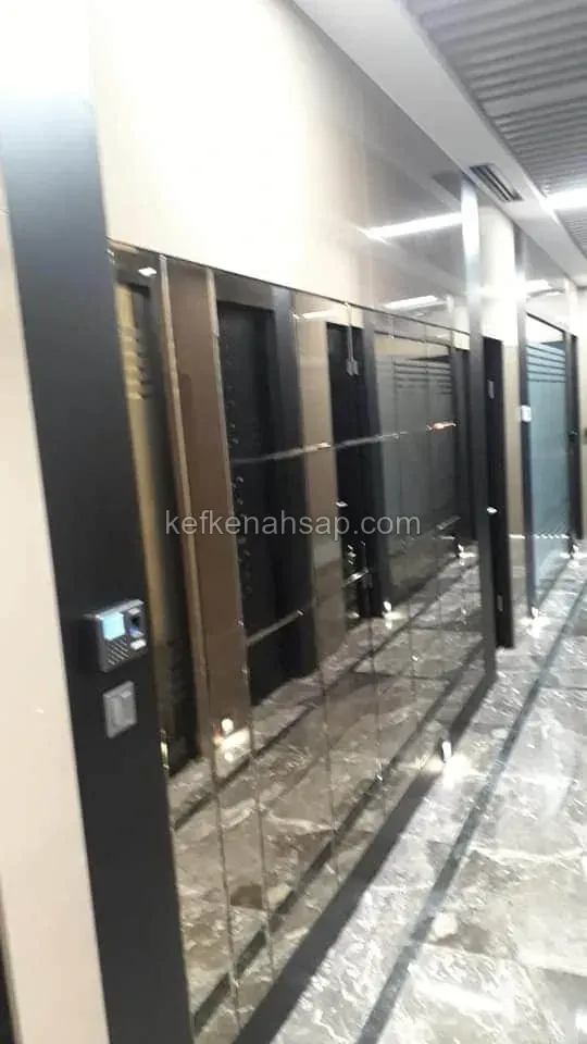 Mermer zeminli koridorda bronz ayna panellerle kaplı duvar, yanında siyah çerçeveli kapılar ve parmak izi okuyucu