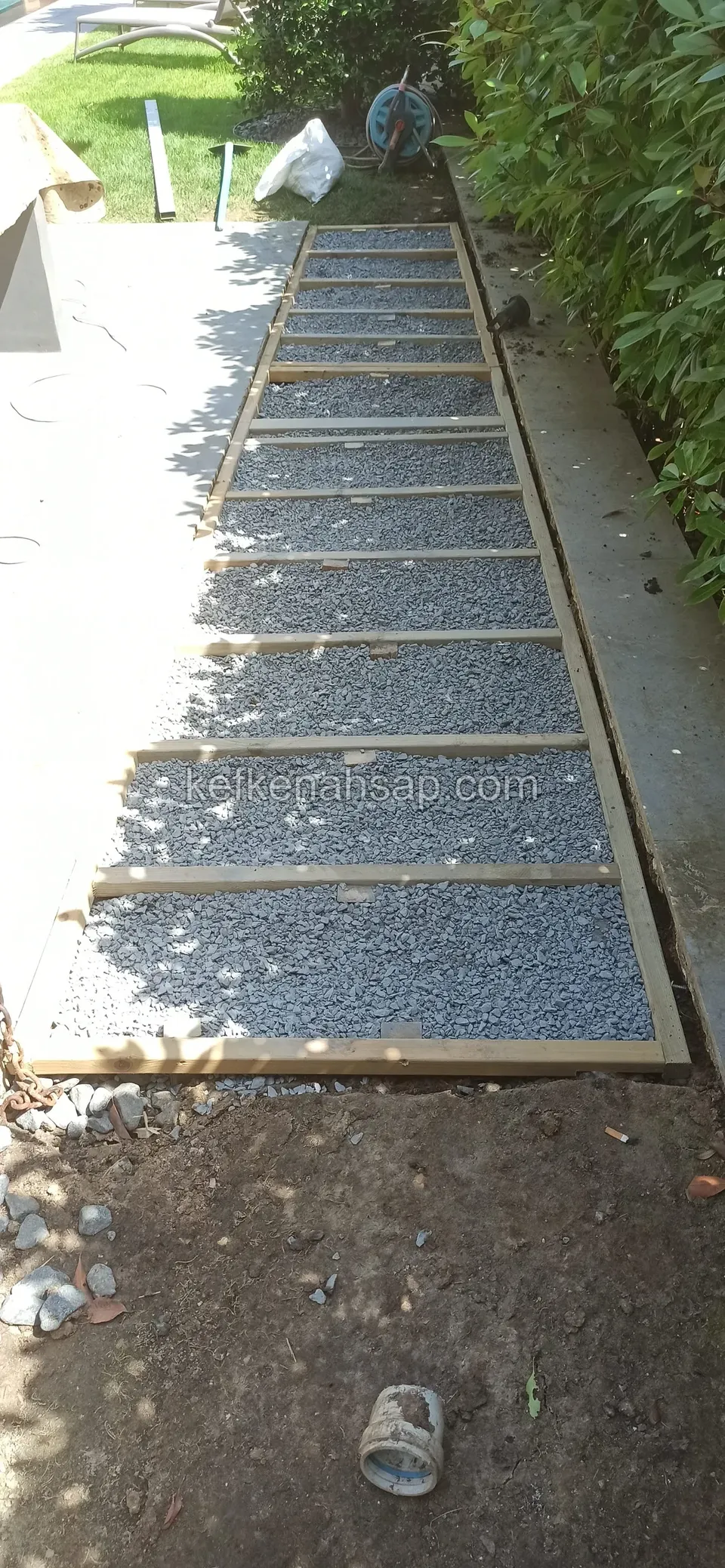 Timber deck frame in a side garden passage, made of cross battens with gravel spread between them