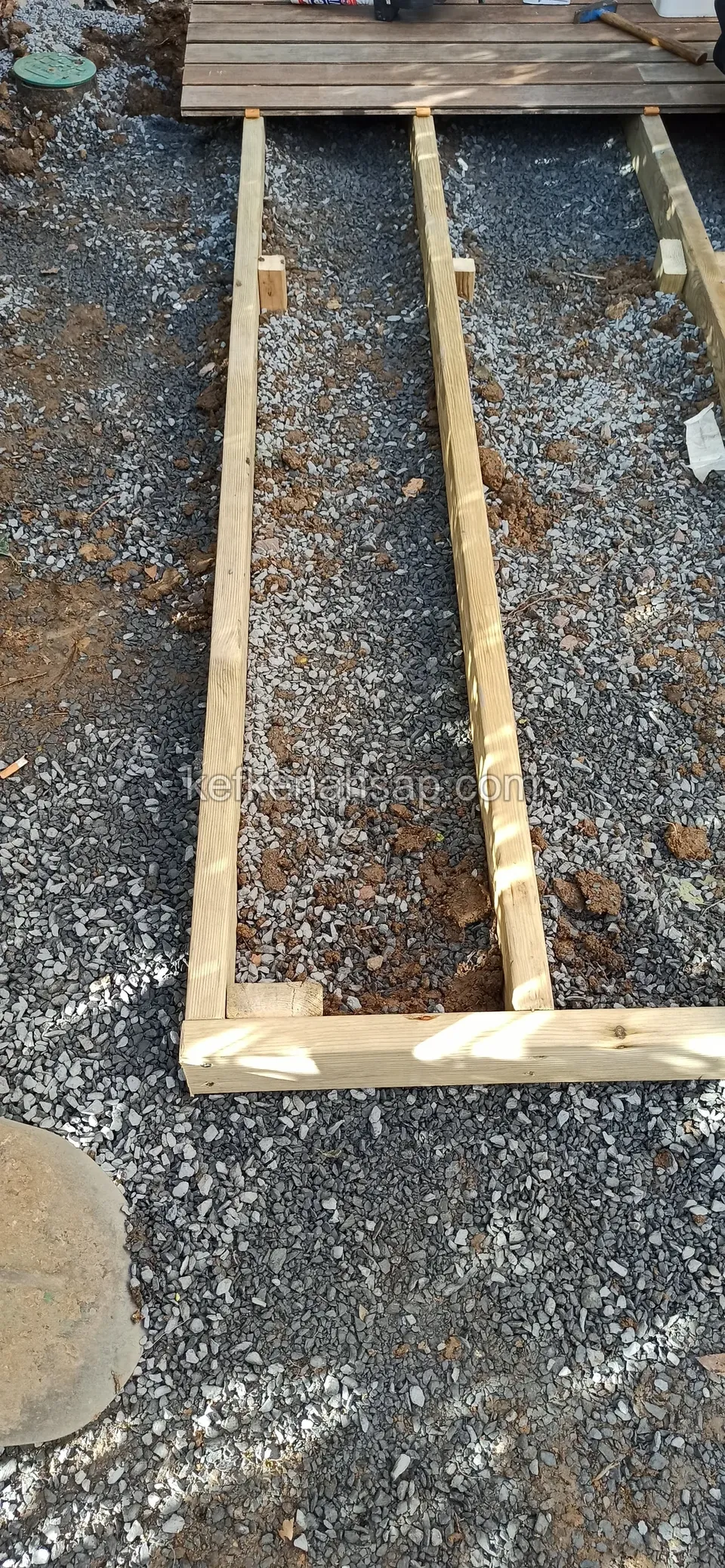 Çakıl serili zeminde yan yana duran iki uzun kiriş ve araya çakılmış kısa çaprazlar, ucunda başlamış deck tahtaları