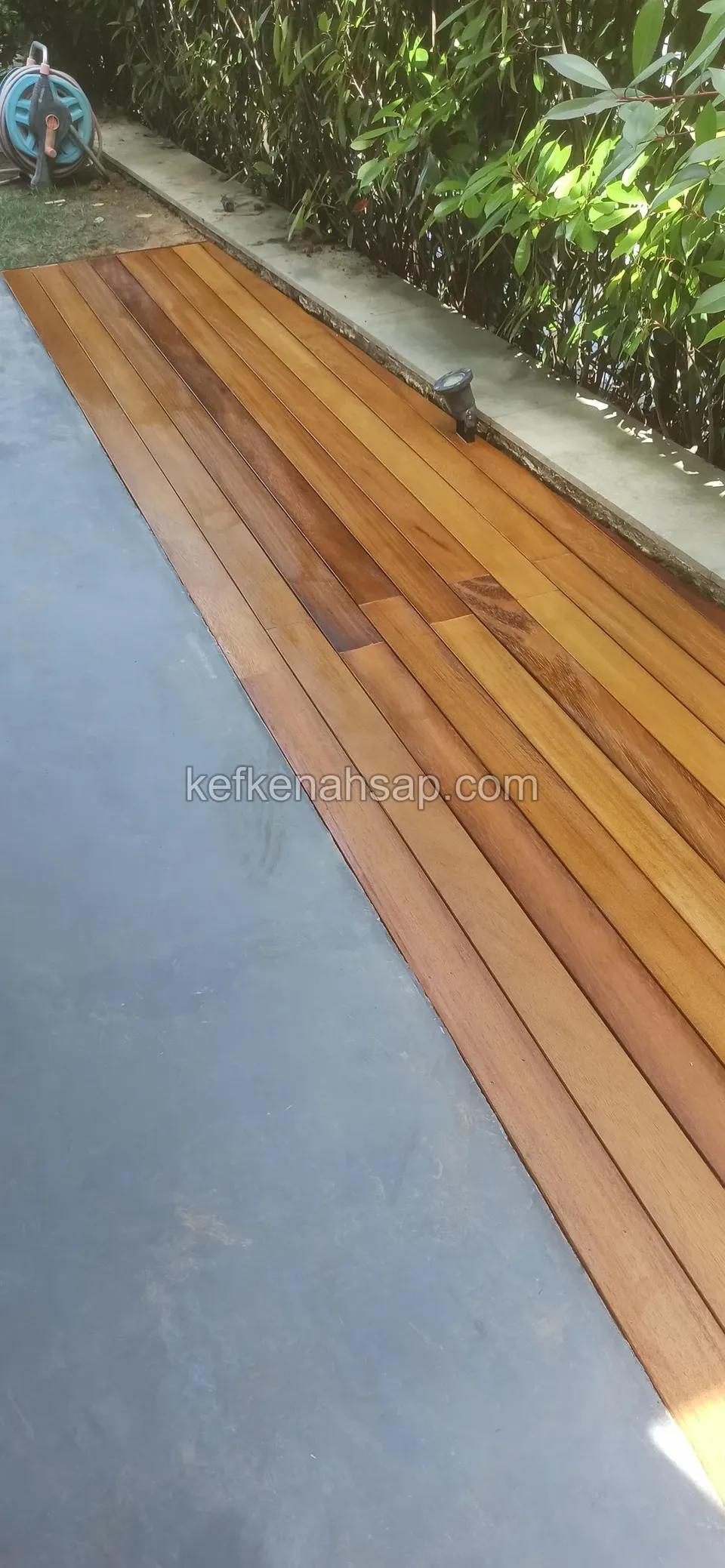 Beton zeminde çalıların yanından uzanan dar deck yolu, kenar bordürde gömülü iki spot lamba