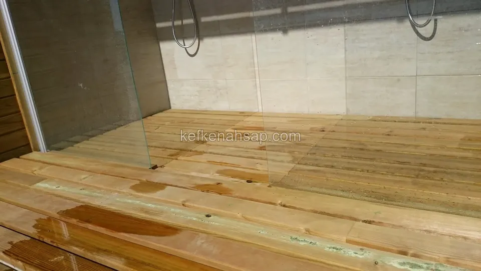 أرضية ديكينغ جديدة بلون العسل في منطقة دش تحت حاجز زجاجي وعلى السطح بقع زيت رطبة وداكنة