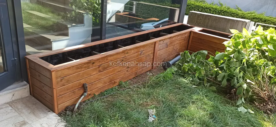 Long varnished timber planter with horizontal slats running beside a lawn in front of a glass wall
