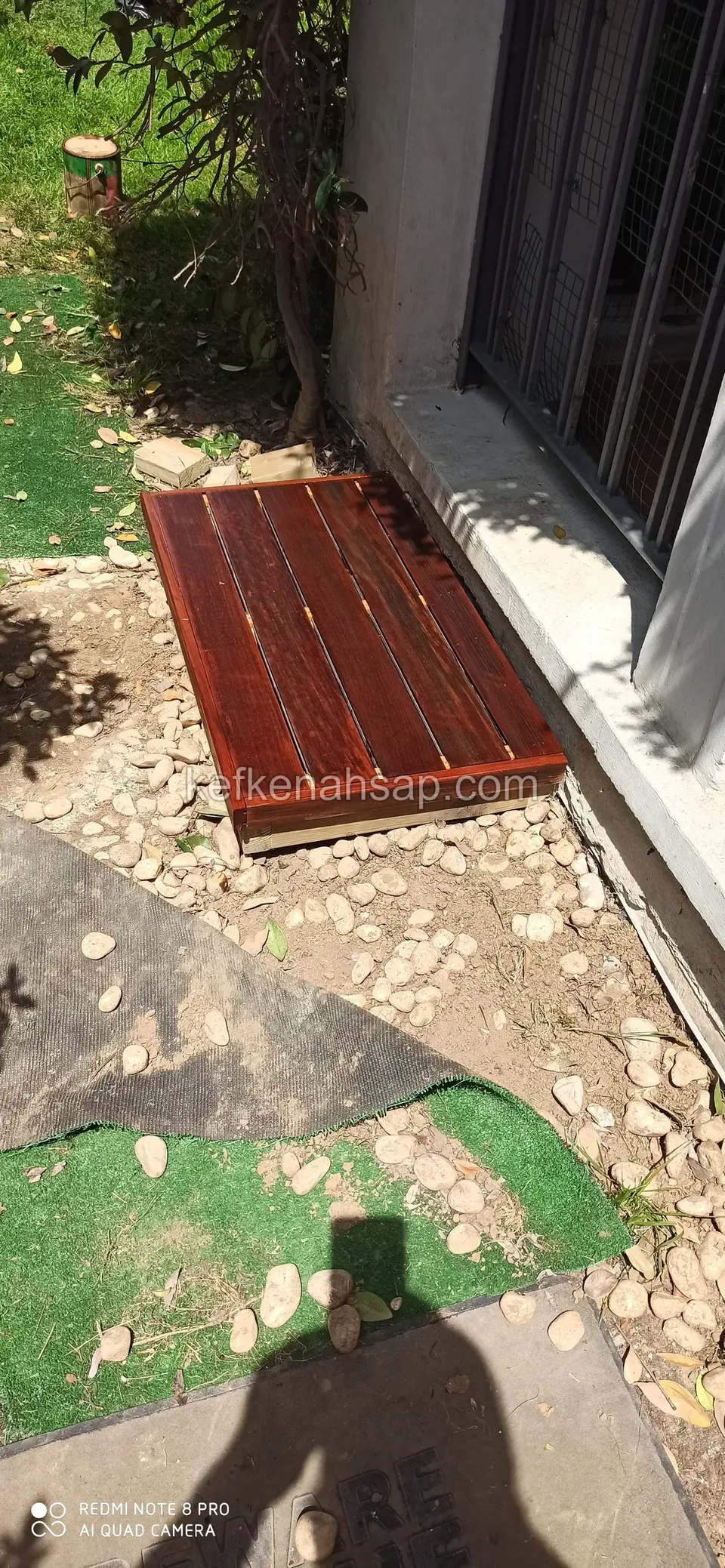 Small red-brown varnished timber platform set among stones in front of a glass door