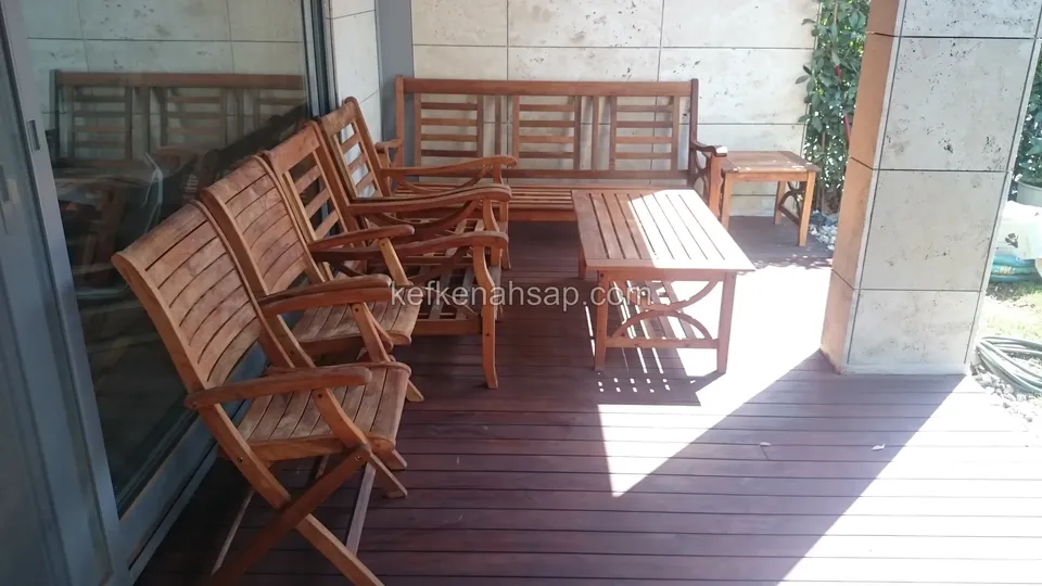 Auf einer Terrasse mit dunklem Holzdeck vor einer Glastür stehen drei braun lackierte Holzsessel