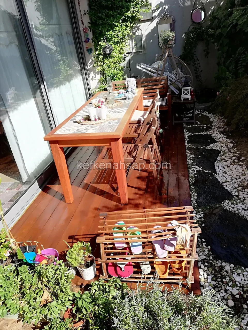 Timber deck in front of a glass door, with a table, a wooden shoe rack and potted plants