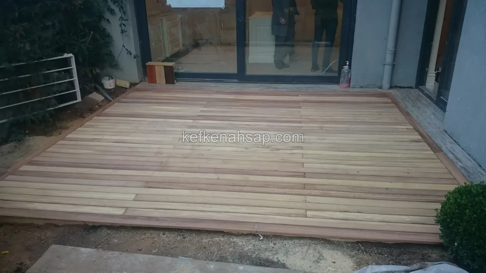 Timber deck laid in front of a glass door, with soil and a shrub visible at its edges