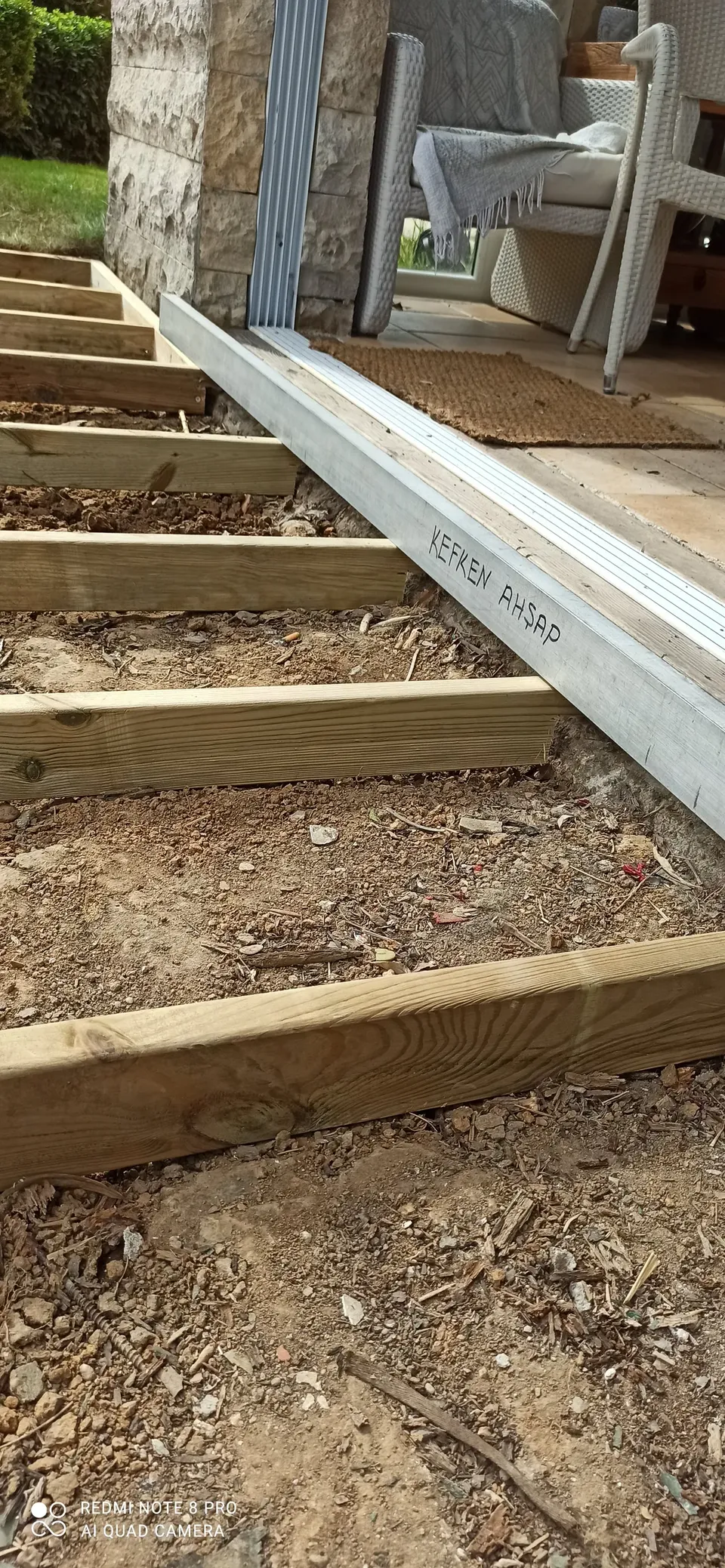 Thick timber joists laid on soil in front of a glass door, with an aluminium profile along the threshold