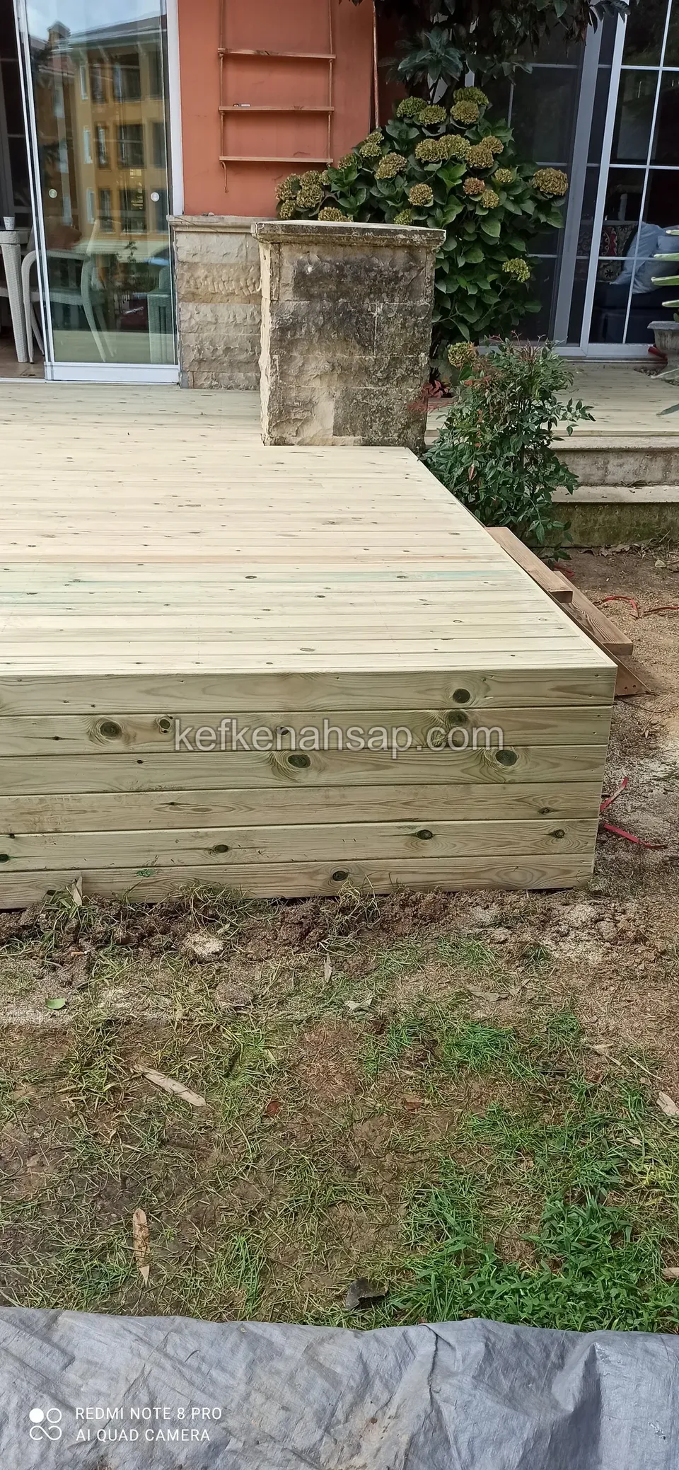 Raised, untreated pale timber deck with side cladding in front of a glass door