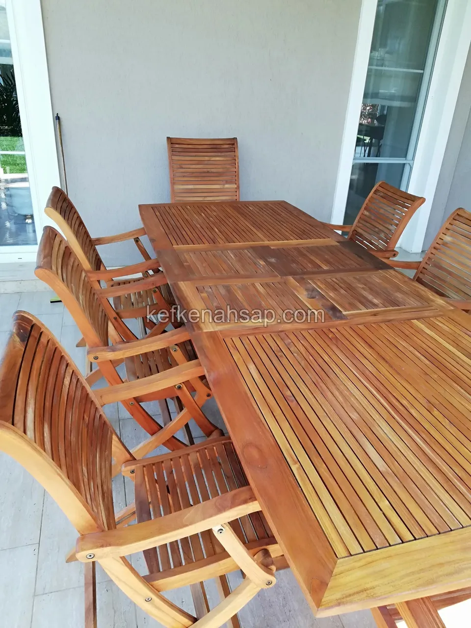 Auf der Terrasse eines Hauses mit Glastüren ein Lattenesstisch aus Holz mit Ausziehplatten und Klappstühlen