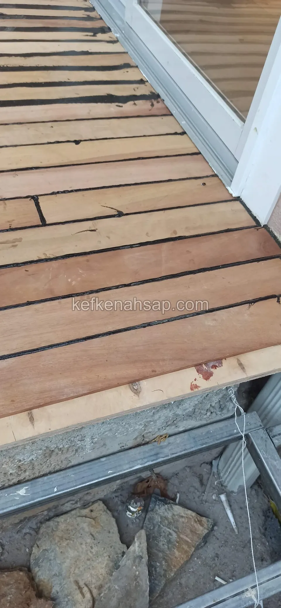 Cam kapı yanında deck kenarı, altta boşluk, taşlar ve metal profil görünüyor