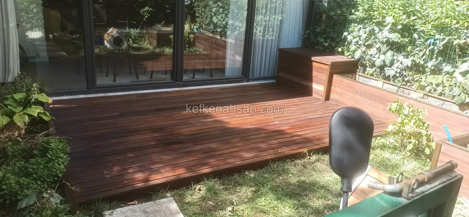 Dark brown deck stretching in front of wide glass doors with a timber bench in the corner and part of a chair in front