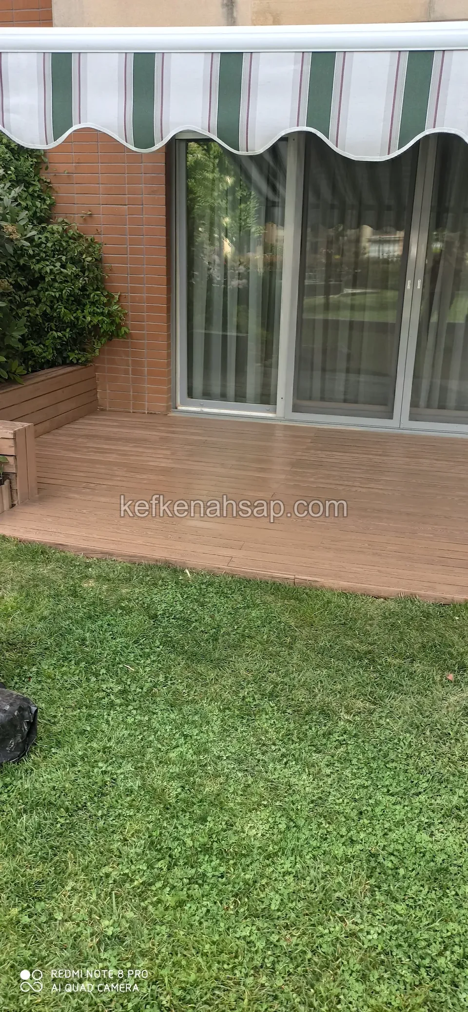 Cam kapılı, tenteli girişin önünde çimene bakan açık kahverengi deck şeridi