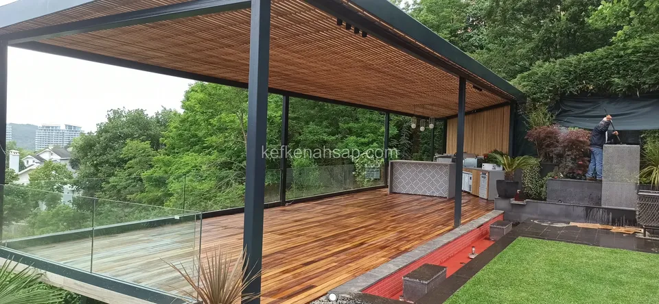Wide terrace with a glass railing, metal frame, slatted timber ceiling, warm-toned deck floor and a lawn