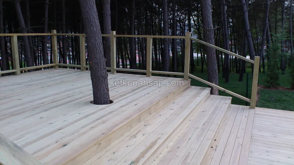 Helle Terrasse um einen Baumstamm im Kiefernwald, am Rand Stufen und ein Holzgeländer aus dünnen Latten
