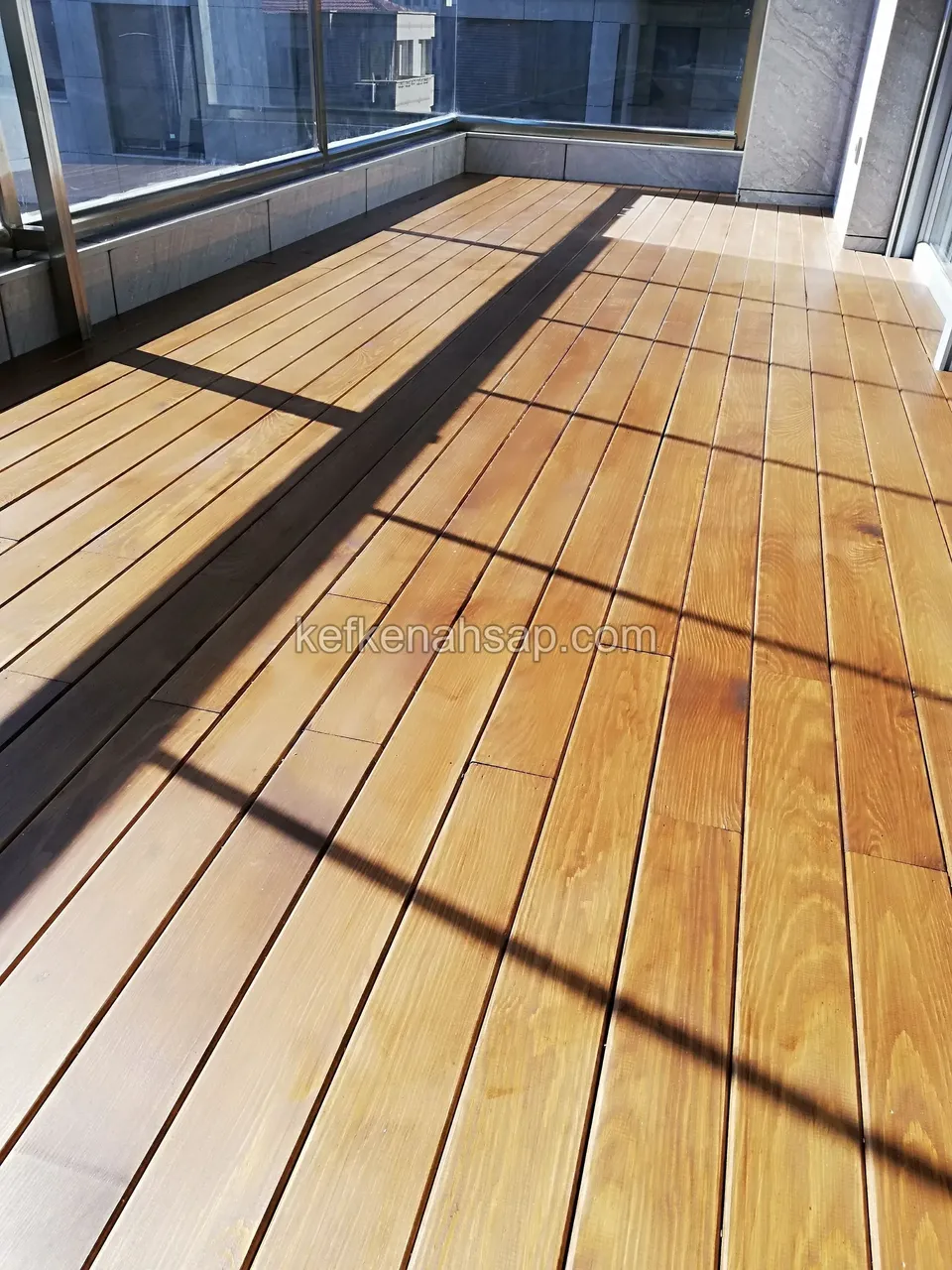 Yellow-brown timber deck boards laid into the corner of a glazed balcony