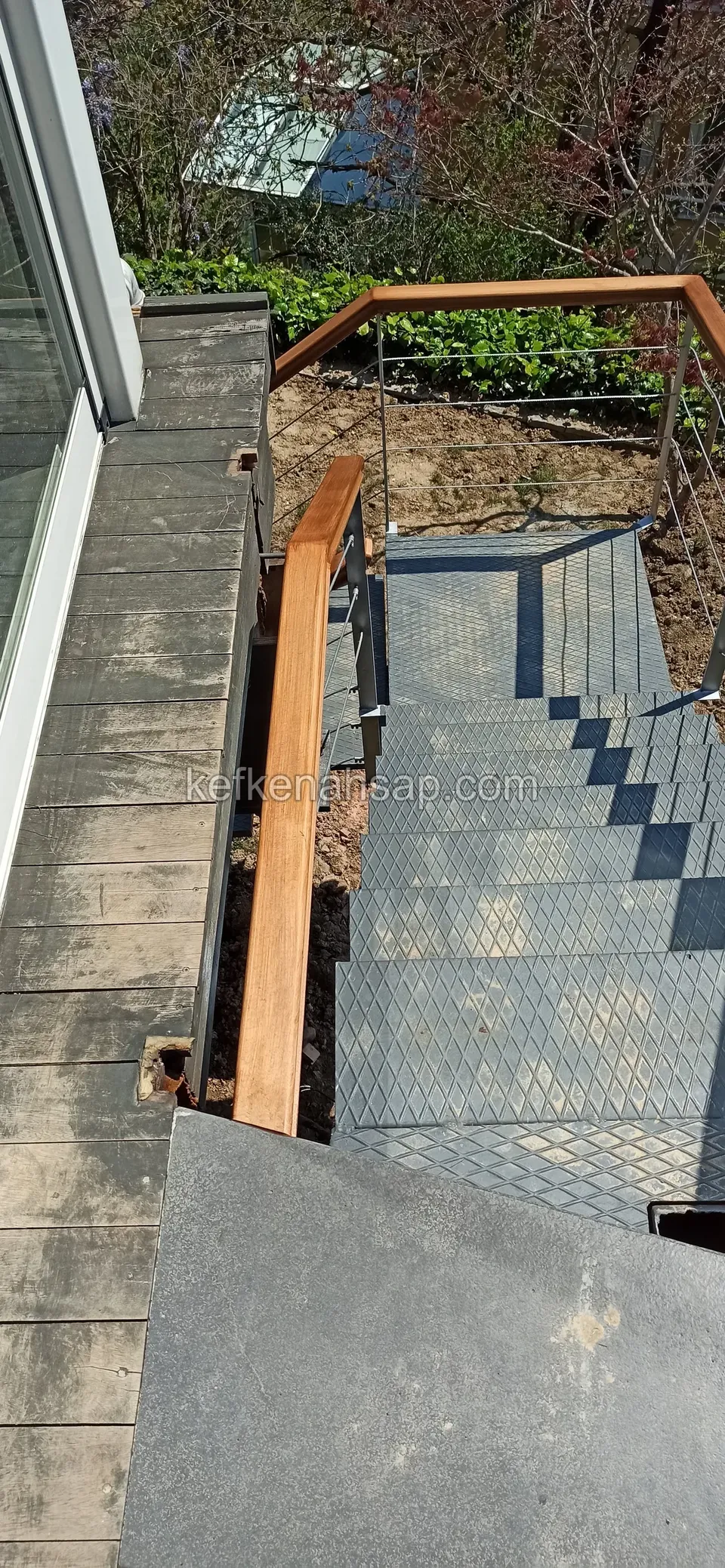 Camlı binanın yanında yukarıdan görünen koyu renkli desenli metal basamaklar ve ahşap küpeşte