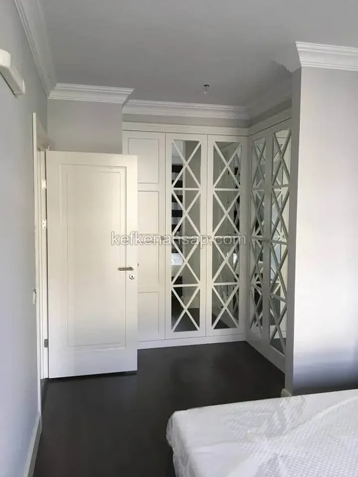 Weiß gestrichener Eckkleiderschrank im Schlafzimmer, Türen mit Spiegeln und Diagonallatten, daneben eine weiße Füllungstür