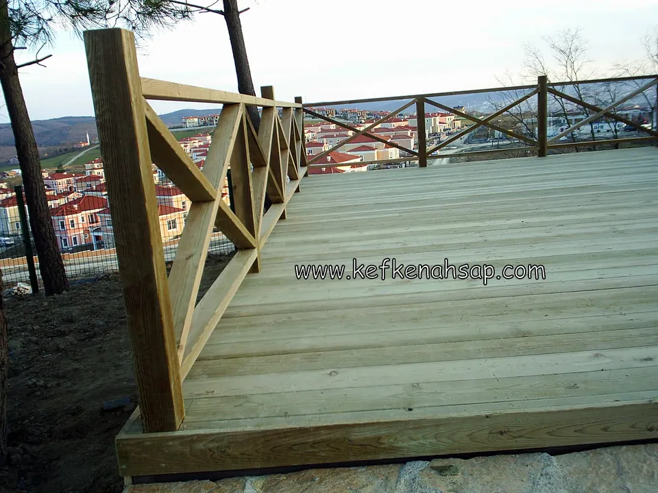Wide, unfinished pale pressure-treated pine deck with a cross-braced timber railing, a residential area visible behind